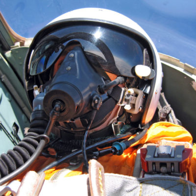 military pilot in the plane in a helmet in dark blue overalls ag military pilot in the plane in a helmet in dark blue overalls against the blue sky